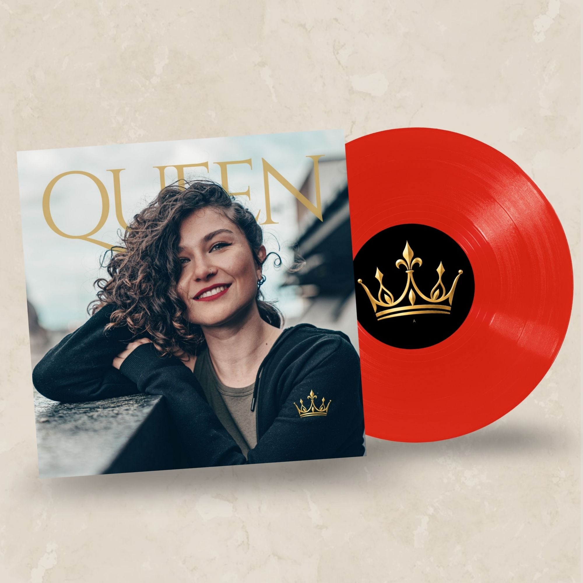 A red vinyl record partially pulled from its album cover, featuring a portrait of Queen with the word 'QUEEN' in large gold letters and a gold crown logo on the record center label.