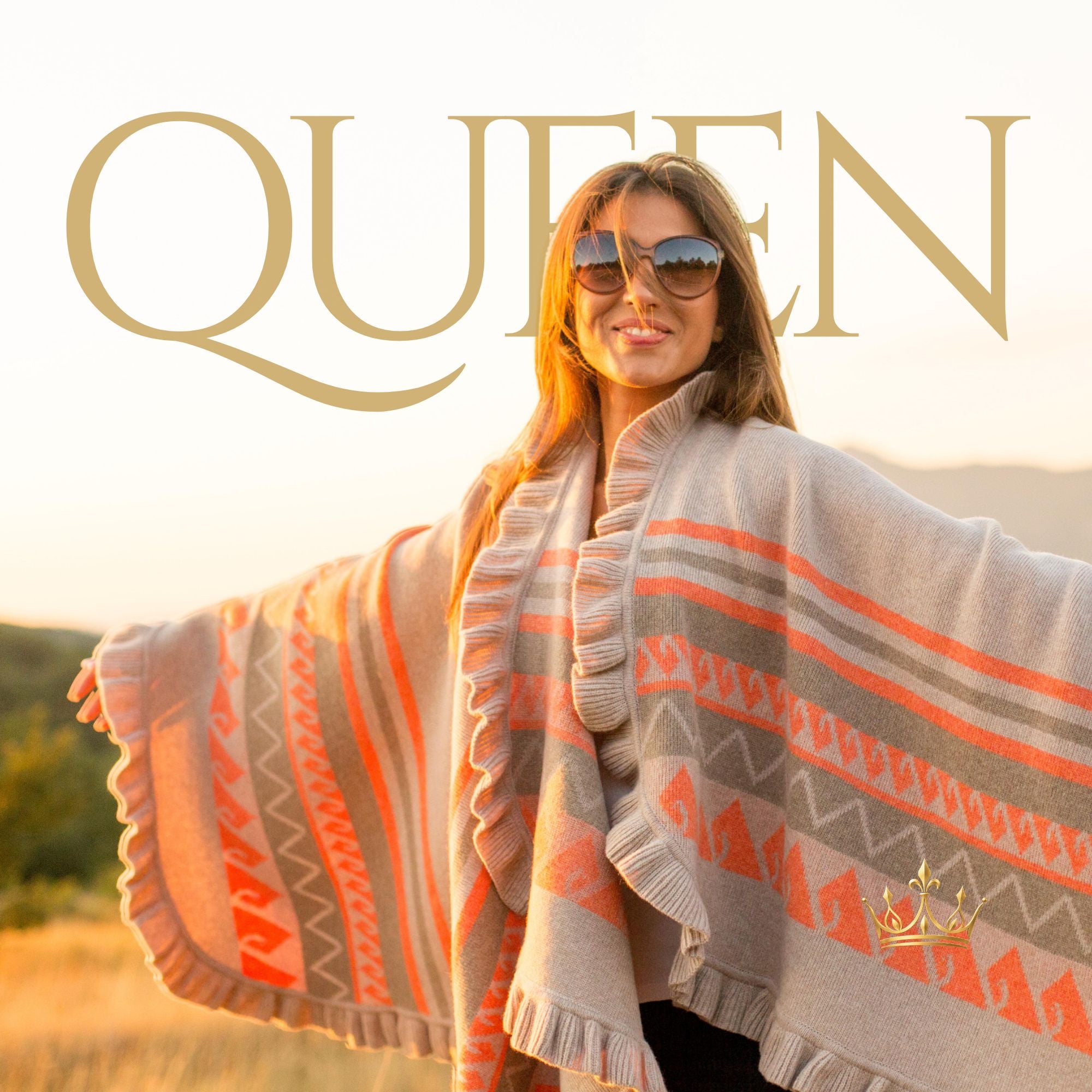 A woman outdoors wearing a large fringed poncho with geometric Southwestern-style stripes in orange, beige, and gray. The word 'QUEEN' appears in large gold letters across the top, and a small gold crown logo is near the lower right.